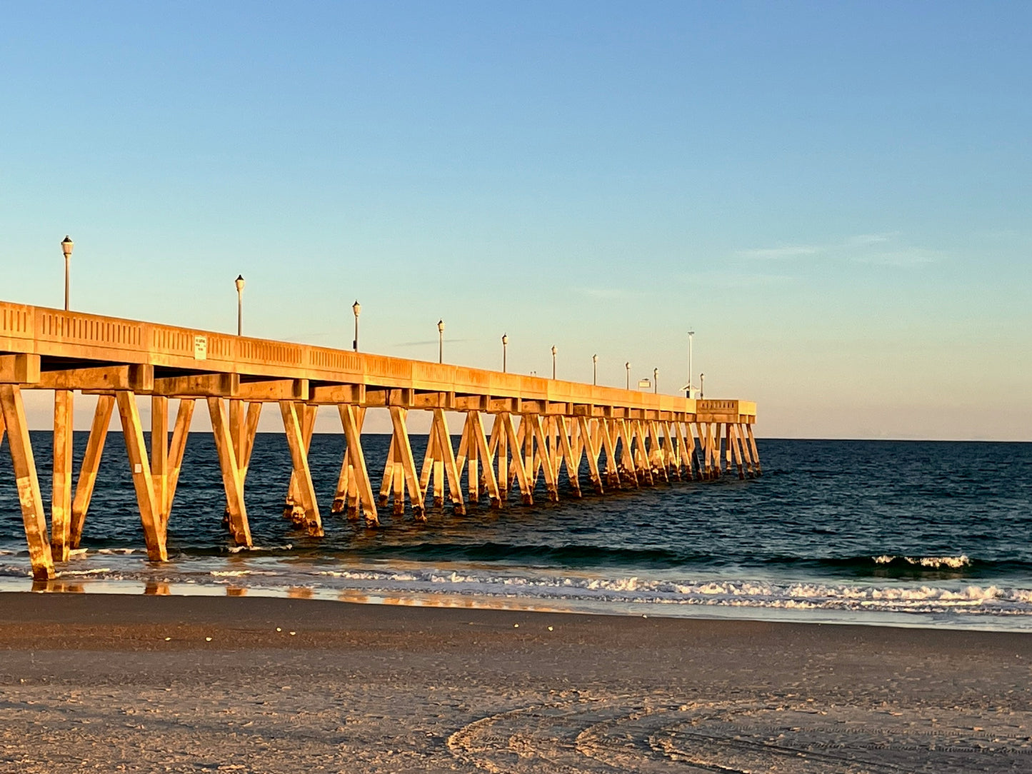 Long wooden pier extending into the ocean with a clear blue sky.